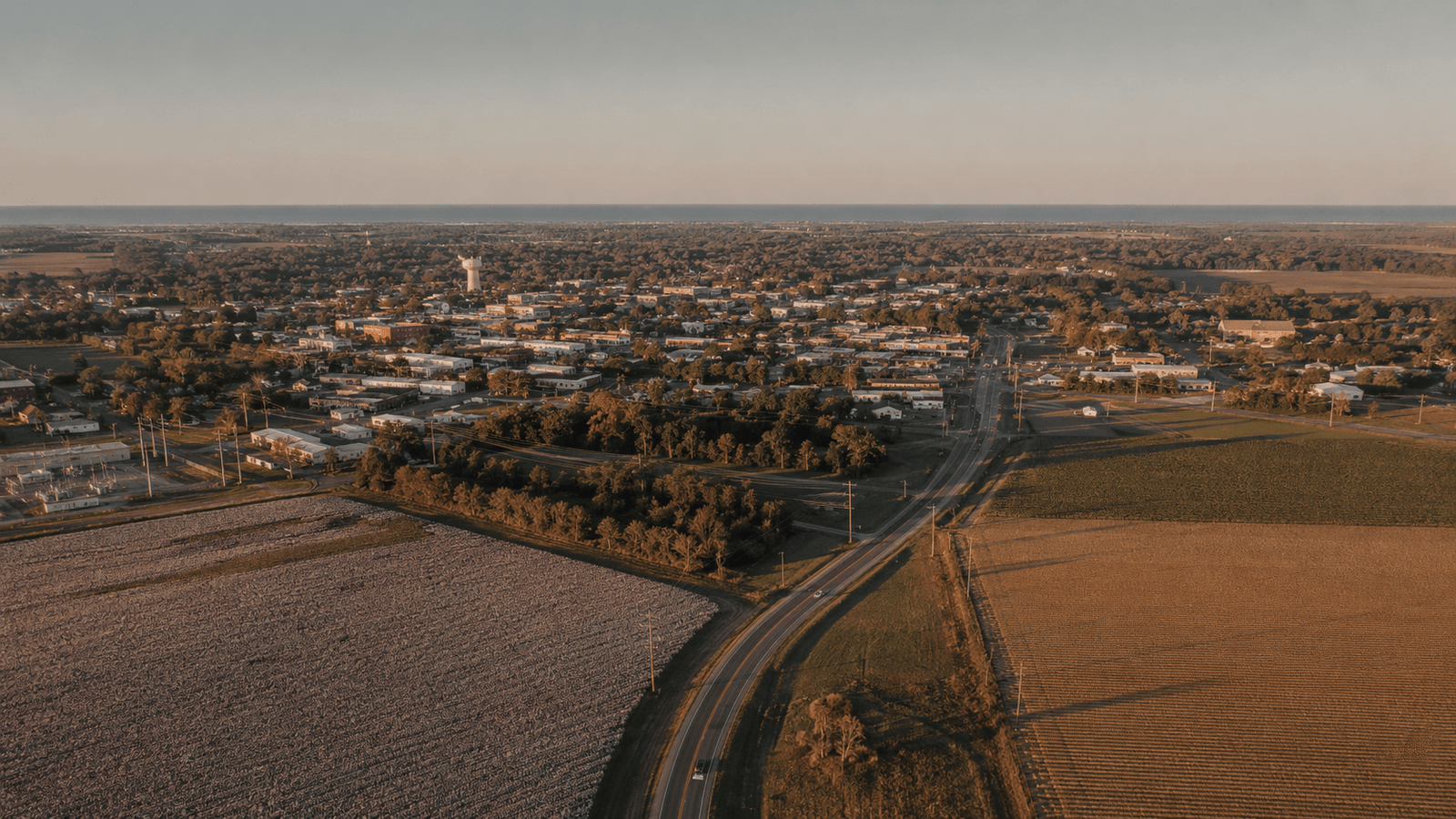 Late afternoon view of the Florida Panhandle and Alabama Wiregrass region — open agricultural land, two-lane highway, warm sky.